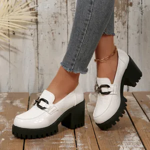 Detail van witte loafers met reliëf, grove zwarte platformhakken en metalen gespen.