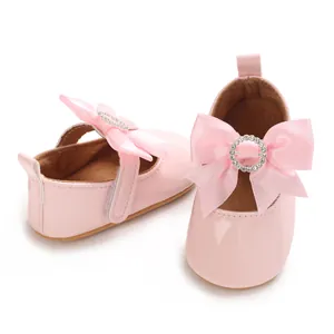 Close-up of pink baby toddler shoes featuring a large ribbon bow and rhinestone buckle detail