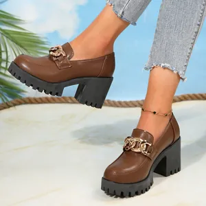 Detail van bruine plateau loafers met gouden ketting en blokhak gedragen door een model.