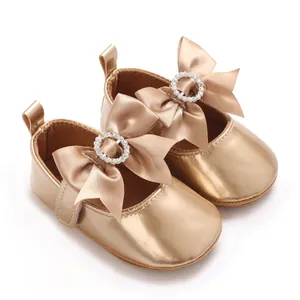 Close-up of champagne gold baby Mary Jane shoes with bow and rhinestone detail