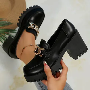 Detailopname van zwarte leren loafers met dikke blokhak en goudkleurige ketting