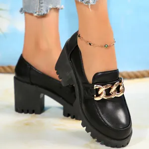 Close-up van stijlvolle zwarte loafers met dikke hak, gouden ketting en plateauzool