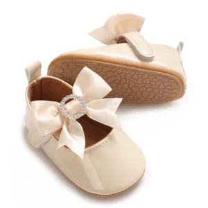 Elegant cream baby shoes with satin bow and rhinestone buckle detail for infants.