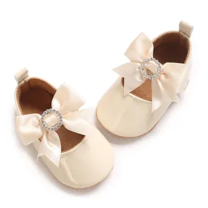 Detail of cream baby shoes featuring a large silk ribbon bow and rhinestone buckle.