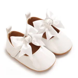 Detail of white baby shoes featuring a large satin bow with sparkling rhinestone circle