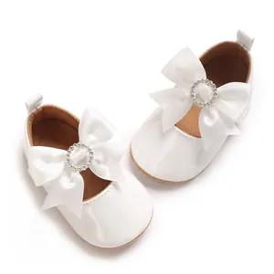 Detailed view of elegant white baby shoes featuring large ribbon bows and rhinestone accents