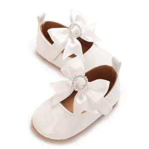 Macro detail of white baby walking shoes with satin bow and rhinestone embellishment