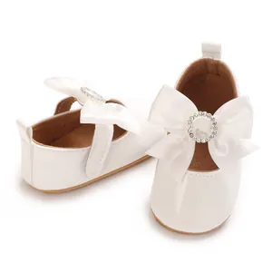 Close-up detail of white patent leather baby girl shoes with large satin rhinestone bow