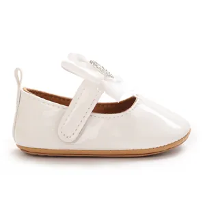 Detailed side view of a white patent leather baby girl shoe with a rhinestone bow