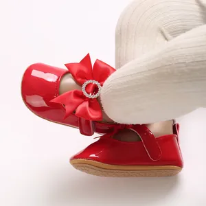 Nahaufnahme von roten Baby-Lackschuhen mit Seidenschleife und glitzernder Strass-Schnalle.