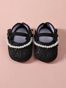 Detailaufnahme der schwarzen Baby-Prinzessinnenschuhe mit eleganten Kunstperlen und Schleifen.