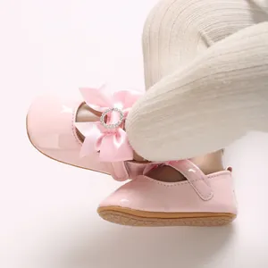 Close-up of pink baby walker shoes with a decorative silk bow and rhinestone buckle.