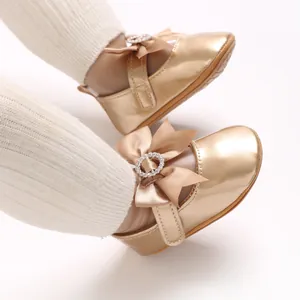 Close-up of champagne gold baby shoes with bow and rhinestone buckle detail