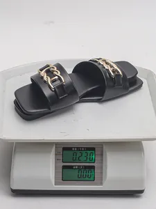 Detailed shot of a black flat sandal with a gold chain buckle being weighed on a digital scale
