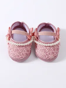 Detailansicht von rosa Spitzen-Babyschuhen mit Perlen- und Schleifenverzierung