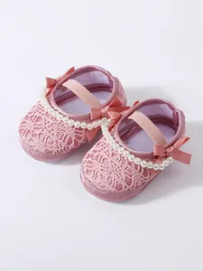 Nahaufnahme rosa Spitzen-Babyschuhe mit Perlensträngen und eleganten Satinschleifen