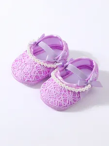 Nahaufnahme eleganter lila Baby-Prinzessin-Schuhe aus Spitze mit Perlenbesatz und Schleifen