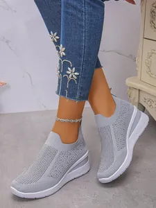 Nahaufnahme grauer Fly-Knit Keilsneaker mit Strasssteinen, getragen von einem Modell.