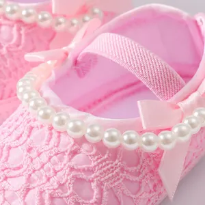 Detailansicht eleganter rosa Baby-Prinzessinenschuhe mit Spitze und Perlenbesatz.