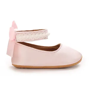 Close-up view of pink baby girl princess shoes with pearl strap and satin bow.