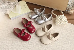Group display of girls' bow Mary Jane shoes in silver, red, and beige on textured rug.