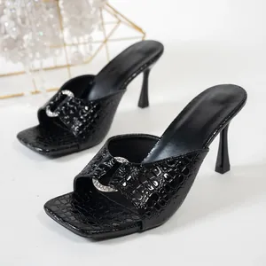 Gros plan sur des sandales noires à talons hauts, motif crocodile et anneau strass