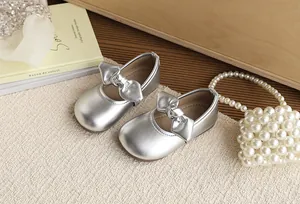 Elegant silver girl's bow princess shoes with soft soles on a textured beige background