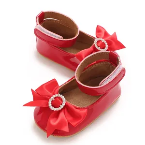 Détail de chaussures de princesse rouges pour bébé avec un grand nœud en satin et strass.