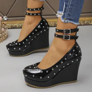 Detalle de zapatos de cuña en charol negro con tachuelas plateadas y doble hebilla