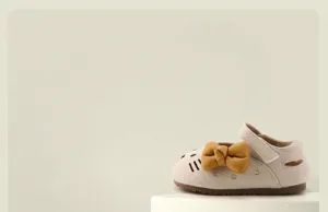 Close-up of baby girl's cream toddler shoe with a yellow bow and cat embroidery