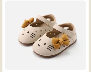 Detail view of cream toddler girl walker shoes featuring a cute cartoon cat face and yellow bow.