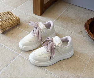 Close-up view of white children's sports shoes with pink laces on a neutral tile floor