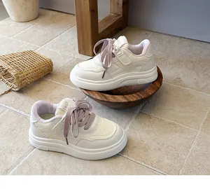 Detailed view of girls white sneakers with pink laces on a tiled floor and wooden bowl
