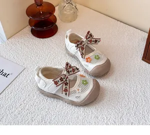 Primer plano de zapatos de malla blanca para niñas con lazo floral y bordado decorativo.