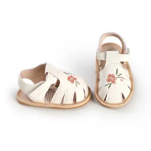 Detail of white soft-sole baby girl sandals with delicate pink floral embroidery and velcro