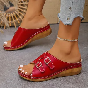 Detail view of red faux leather wedge slides featuring double buckles and stitching.