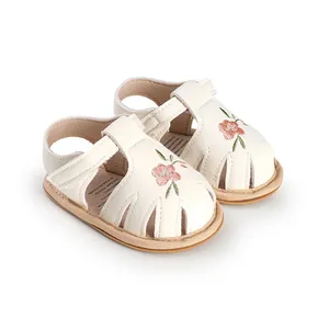 Close-up of white baby girl sandals with delicate floral embroidery and soft soles