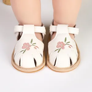 Close-up of white baby walking sandals with pink flower embroidery details.
