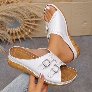 Detailed view of white wedge slippers featuring dual buckle straps and decorative cutouts