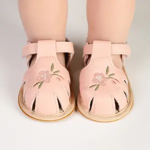 Detailed close-up of pink embroidered baby sandals on doll feet with T-strap design