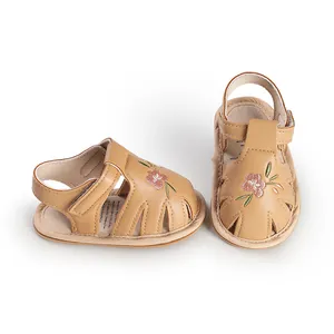 Detail view of tan baby girl sandals with embroidered pink flowers and hook-and-loop strap.