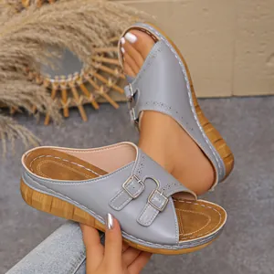 Close-up of grey wedge sandals featuring dual buckles and elegant laser-cut details