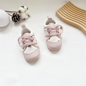 Detail of baby girl walking shoes with strawberry pattern and pink ribbon bow velcro strap.