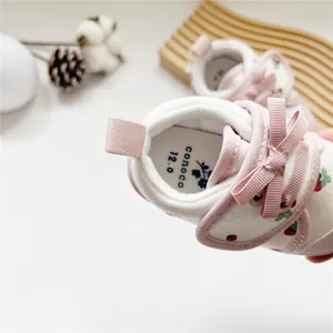 Detailed macro view of pink baby girl walking shoe with strawberry print and bow.