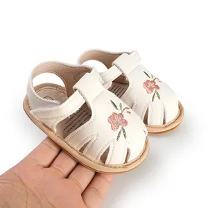 Detailed view of white infant walking sandals with embroidered flowers for baby girls.