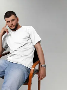 Detail view of a men's plain white drop shoulder t-shirt in a comfortable sitting pose