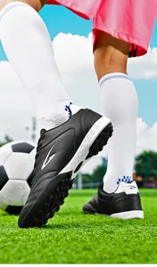 Close-up of black breathable TF turf soccer shoes on a green field during training.