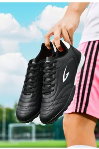 Close-up of black turf soccer shoes with white logo held against a bright soccer field