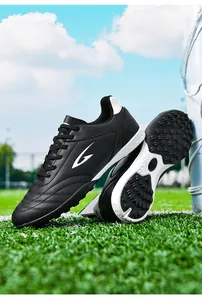 Professional black TF soccer cleats with turf studs shown on a green football field