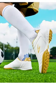 Close-up of white soccer shoes featuring gold accents and TF turf cleats on a field.